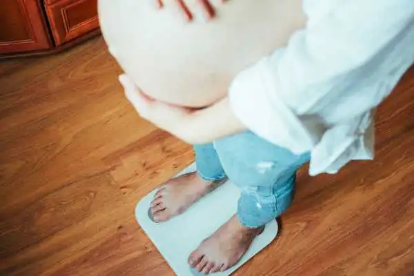 Image of woman weighing herself and experiencing weight gain through pregnancy Underwood